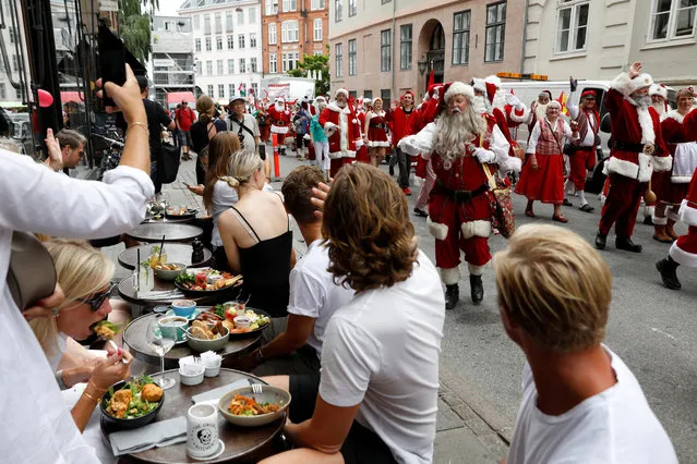 Diners react as a parade of people dressed as Santa Claus pass by during the World Santa Claus Congress, an annual event held every summer in Copenhagen, Denmark, July 23, 2018. (Photo by Andrew Kelly/Reuters)