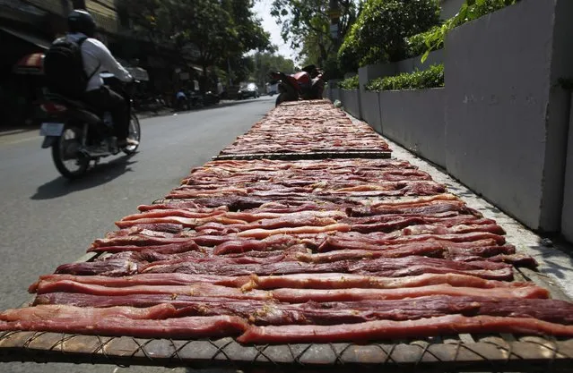 A man rides a motorcycle near dried buffalo meat laid out by a shopkeeper, along a street in central Phnom Penh February 9, 2015. The dried buffalo meat is sold for $2.50 per plate, according to the shopkeeper. (Photo by Samrang Pring/Reuters)