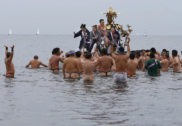 Participants cheer on a portable shrine carried by others as they parade through the sea during a mid-winter festival at Enoshima beach in Fujisawa, west of Tokyo, Sunday, January 17, 2016. The annual festival is held to celebrate youths coming of age this year as well as to pray for the safety of the portable shrines. (Photo by Shizuo Kambayashi/AP Photo)