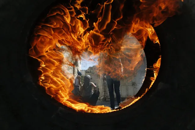 Palestinian protesters are seen through a burning tyre during clashes with the Israeli soldiers after the Friday prayers in the centre of the occupied West Bank city of Hebron on July 27, 2018. (Photo by Hazem Bader/AFP Photo)