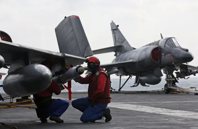 Red jacket ordnance crew equip a Super Etendard fighter jet with a missile near a Rafale fighter jet aboard France's Charles de Gaulle aircraft carrier in the Gulf, January 29, 2016. (Photo by Philippe Wojazer/Reuters)