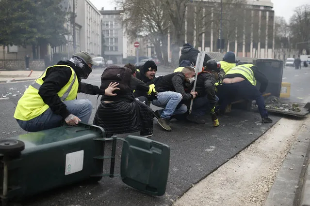 Yellow vest demonstrators take cover during clashes with French riot police during a demonstration in Bourges, central France, Saturday, January 12, 2019. Paris brought in armored vehicles and the central French city of Bourges shuttered shops to brace for new yellow vest protests. The movement is seeking new arenas and new momentum for its weekly demonstrations. Authorities deployed 80,000 security forces nationwide for a ninth straight weekend of anti-government protests. (Photo by Rafael Yaghobzadeh/AP Photo)