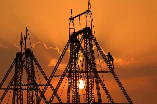 A labourer is silhouetted against the setting sun as he works on a columbus swing at a fair ground in Pushkar, India on November 5, 2023. (Photo by Himanshu Sharma/AFP Photo)