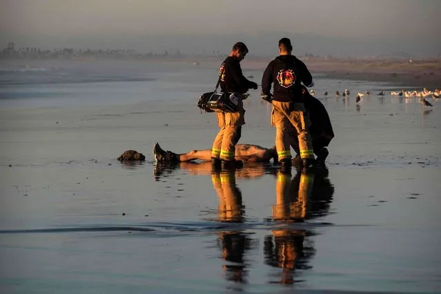 US Border Patrol agents look at the body of a dead migrant, allegedly from Russia, who appeared on the beach in the US after drowning while trying to cross the US-Mexico border, seen from Playas de Tijuana, Mexico, on November 9, 2022. (Photo by Guillermo Arias/AFP Photo)