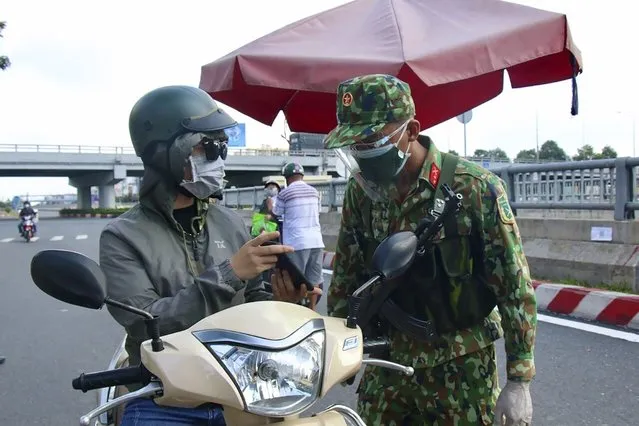 An army soldier checks identifications at a COVID-19 lockdown checkpoint in Ho Chi Minh City, Vietnam, Monday, August 23, 2021. Vietnam's largest metropolis Ho Chi Minh City has enabled a strict lockdown order to help curb the recent outbreak of the pandemic. (Photo by Vu Tien Luc/VNA via AP Photo)