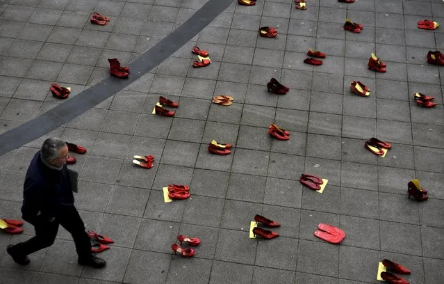 A man walks past a group of red shoes used for a performance to denounce violence against women organized by Amnesty International during International Women's Day in Gijon, Spain, March 8, 2016. (Photo by Eloy Alonso/Reuters)