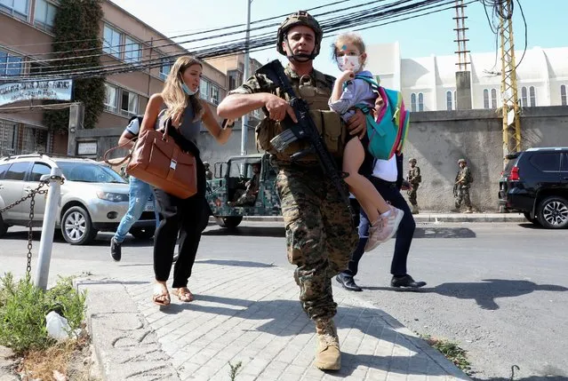An army soldier carries a schoolchild as civilians flee after gunfire erupted at a site near a protest that was getting underway against Judge Tarek Bitar, who is investigating last year's port explosion, in Beirut, Lebanon on October 14, 2021. (Photo by Mohamed Azakir/Reuters)