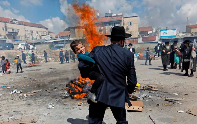 An Ultra-Orthodox Jewish man carries a child near burning leavened items during the Biur Chametz ritual on April 19, 2019 in Jerusalem, on the eve of the Jewish Pesach (Passover) holiday, which begins at sunset today. Due to the haste with which the Jews left Egypt, the bread they had prepared for the journey did not have time to rise To commemorate their ancestors' plight, the religious avoid eating leavened food products throughout Passover. (Photo by Menahem Kahana/AFP Photo)