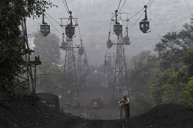 A worker pushes his bicycle under a line of cable trolleys transporting coal in Sonbhadra, Uttar Pradesh, on November 19, 2021. (Photo by Money Sharma/AFP Photo)