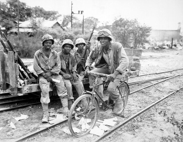 Members of the U.S. Marine Corps, Corporal Willis T Anthony, Private First Class Emmitt Shackelford, and Private First Class Eugene Purdy, and Private First Class Horace Boykin (riding bicycle)) attached to the Third Ammunition Company, take time out from supplying ammunition to the front line on Saipan, Northern Mariana Islands, in June of 1944. (Photo by National Archives)