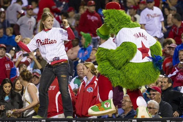 This September 16, 2013. file photo shows the Phillies Phanatic dancing with a fan on the dugout during the eighth inning of a baseball game in Philadelphia. The Philadelphia Phillies have sued the New York company that created the Phanatic mascot to prevent the green fuzzy fan favorite from becoming a free agent. In a complaint filed Friday, August 2, 2019, in U.S. District Court in Manhattan, the team alleged Harrison/Erickson threatened to terminate the Phillies' rights to the Phanatic next year and “make the Phanatic a free agent” unless the team renegotiated its 1984 agreement to acquire the mascot’s rights. (Photo by Chris Szagola/AP Photo/File)