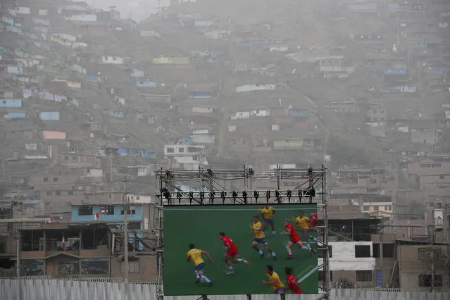 A screen shows action replay of a rugby seven match between Canada and Brazil during the Pan American Games inside a stadium where homes can be seen on the hillside behind in Lima, Peru, Sunday, July 28, 2019. (Photo by Moises Castillo/AP Photo)