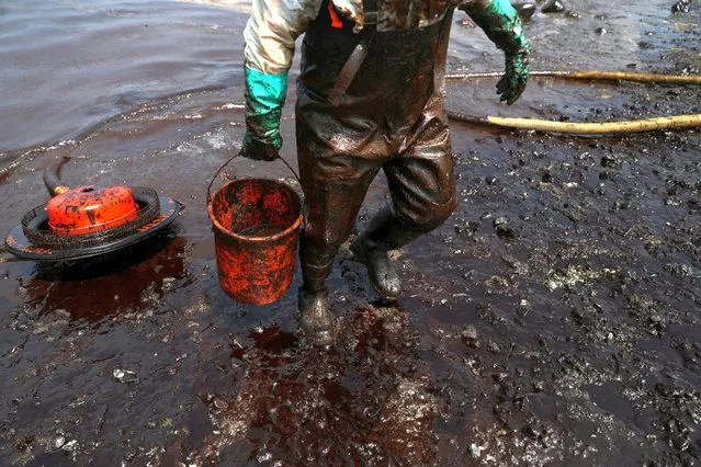 A worker cleans up an oil spill following an underwater volcanic eruption in Tonga, in Ancon, Peru on January 25, 2022. (Photo by Pilar Olivares/Reuters)