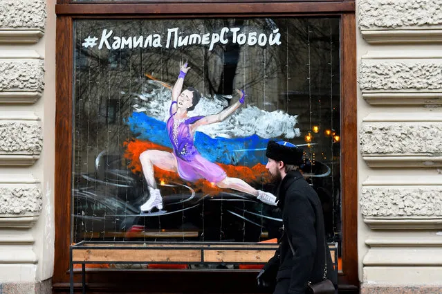 A man walks past a restaurant window with a painting bearing Russia's figure skater Kamila Valieva and reading “Kamila, Petersburg is with you!” in Saint Petersburg on February 16, 2022. Teenage Russian figure skater Kamila Valieva will go for a second Beijing Olympics title on February 17, 2022 the next chapter in a damaging doping scandal which has overshadowed the Games. (Photo by Olga Maltseva/AFP Photo)