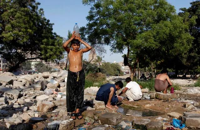 A boy, who collects waste papers for recycling, takes a bath while others wash near a puddle of water at a demolished plot in Karachi, Pakistan, April 26, 2016. (Photo by Akhtar Soomro/Reuters)