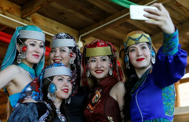 Models of the “Altyr” fashion theatre, dressed in Khakas national costumes, take a selfie during a break in a photo session, as a part of the rehearsal for the Tun-Pairam traditional holiday (The Holiday of the First Milk) celebration at a museum preserve outside Kazanovka village near Abakan in the Republic of Khakassia, Russia, May 28, 2016. The “Khakas aal” (Khakas settlement) ethnographic complex demonstrates the model of a traditional local settlement of the 19th century based on local traditional wooden yurts. The museum preserve is located in a picturesque forest-steppe valley near the Abakan ridge of the Kuznetsk Alatau mountain range and displays numerous objects of the cultural and historical heritage of various epochs accumulated by the people living on this territory, according to representatives. (Photo by Ilya Naymushin/Reuters)