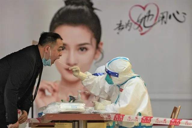 A medical worker in protective gear collects a sample from a worker at a COVID testing site setup outside a shopping mall on Sunday, May 22, 2022, in Beijing. (Photo by Andy Wong/AP Photo)