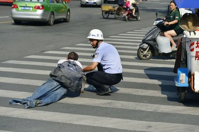 A beggar who lay at the side of a road pretending he had no legs was moved on by police who made him stand up and walk away. The man lay slumped on his front in Chengdu, in Sichuan Province, China, with his legs tucked under him, and his jeans stretched out to make it appear he had no legs. He is approached by a police officer, who bends down and talks to him for some moments. (Photo by Rex Features)