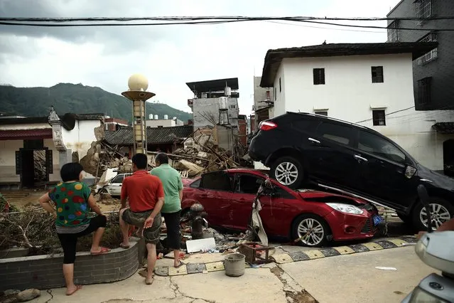 This photo taken on July 10, 2016 shows residents looking at damaged cars and houses in the aftermath of a tropical storm in Bandong town, in Minqing county, east China's Fujian province. (Photo by AFP Photo/Stringer)