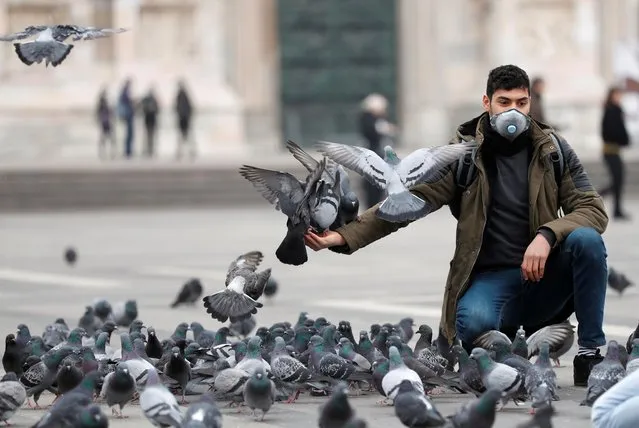 A man in a face mask feeds pigeons in Milan, as the country is hit by the coronavirus outbreak, February 25, 2020. (Photo by Yara Nardi/Reuters)