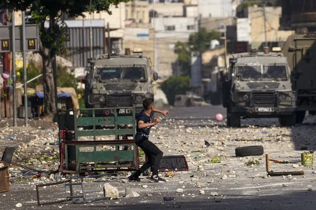 Palestinian demonstrators clash with the Israeli army while forces carry out an operation in the West Bank town of Nablus, Tuesday, August 9, 2022. Israeli police said forces encircled the home of Ibrahim al-Nabulsi, who they say was wanted for a string of shootings in the West Bank earlier this year. They said al-Nabulsi and another Palestinian militant were killed in a shootout at the scene, and that troops found arms and explosives in his home. (Photo by Majdi Mohammed/AP Photo)