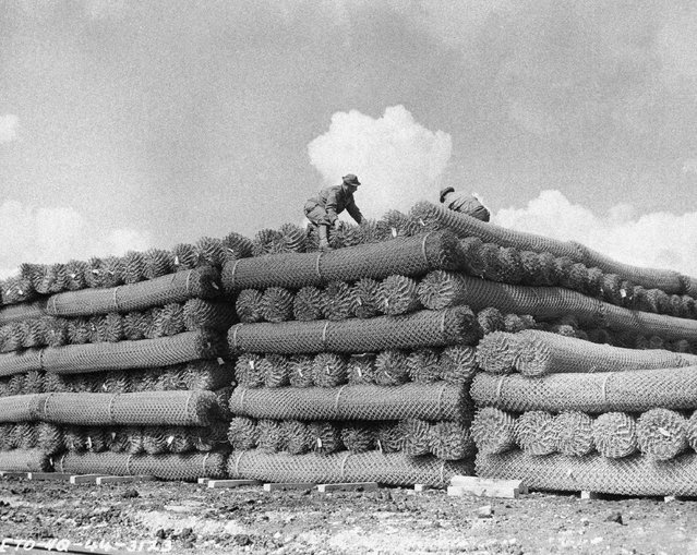 U.S. soldiers pile huge rolls of wire fence at an army supply depot for the coming invasion of the European continent in England, May 15, 1944. Equipment for invasion use has been piling up at ordnance depots all over England. (Photo by AP Photo)