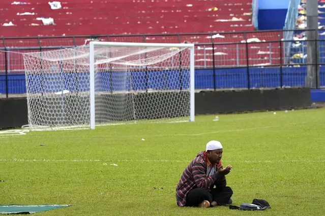 A supporter soccer club Arema FC prays for victims of Saturday's soccer match stampede inside the Kanjuruhan Stadium in Malang, Indonesia, Monday, October 3, 2022. Panic at an Indonesian soccer match Saturday left over 100 people dead, most of whom were trampled to death after police fired tear gas to stop the violence. (Photo by Achmad Ibrahim/AP Photo)
