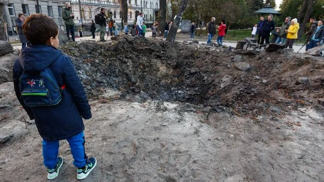 A young boy inspects a crater near a playground in Taras Shevchenko Park in Kyiv on October 12, 2022. People later left flowers in the crater in tribute to those killed during the attack. (Photo by Serhiy Nuzhnenko/Radio Free Europe/Radio Liberty)