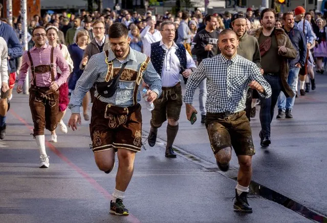 People run onto the festival ground on the opening day of the 187th Oktoberfest beer festival in Munich, Germany, Saturday, September 17, 2022. Oktoberfest is back in Germany after two years of pandemic cancellations, the same bicep-challenging beer mugs, fat-dripping pork knuckles, pretzels the size of dinner plates, men in leather shorts and women in cleavage-baring traditional dresses. (Photo by Michael Probst/AP Photo)
