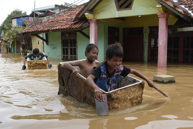 Children use abandoned refrigerators as rafts in a flooded area after heavy rain caused a river overflow, submerging scores of homes in Bandung, West Java, on March 16, 2025. (Photo by Timur Matahari/AFP Photo)