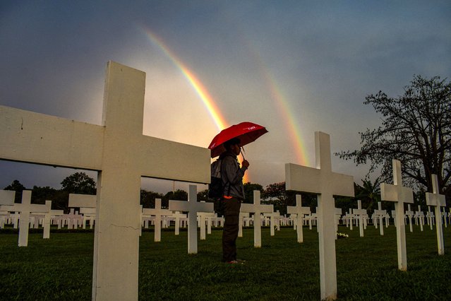 A man holding an umbrella stands besides graves as he looks for the grave of his relative at a cemetery for victims of World War II Ereveld Pandu, in Bandung, on August 15, 2022, as part of the commemoration of the end of World War II in Southeast Asia 77 years ago, on August 15, 1945. (Photo by Timur Matahari/AFP Photo)
