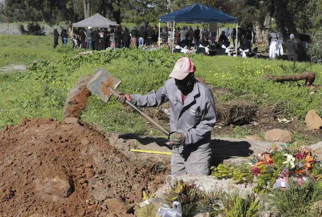A gravedigger works in the COVID-19 section of the Maitland Cemetary in Cape Town, South Africa, Wednesday, July 15, 2020 as a burial takes place in the background. South Africa has surpassed the UK in its number of confirmed coronavirus cases and now has the world's eighth-highest number of confirmed cases at 298,292, which is nearly half of all the confirmed cases on the African continent. (Photo by Nardus Engelbrecht/AP Photo)