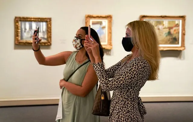 Visitors wearing face masks photograph a painting from the Degas exhibit in the West Building of the National Gallery of Art, which reopened today after months of closure due to the coronavirus disease (COVID-19) outbreak, in Washington, U.S., July 20, 2020. (Photo by Kevin Lamarque/Reuters)