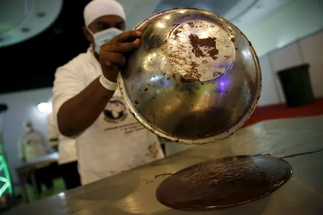 A worker spreads chocolate out on a metal table to cool it off during an attempt to break the Guinness World Record for the biggest chocolate coin in Caracas, Venezuela, October 1, 2015. (Photo by Carlos Garcia Rawlins/Reuters)