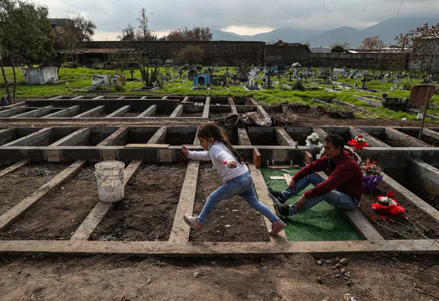 Jose Collantes and his five-year-old daughter Kehity visit the tomb of his wife Silvia Cano, the mother of Kehity, who died of the new coronavirus, one month after burying her at the Catholic Cemetery where they come once a week in Santiago, Chile, Wednesday, August 5, 2020. For many pandemic survivors and those who lost loved ones, the tragedy lingers and their lives are never the same. (Photo by Esteban Felix/AP Photo)