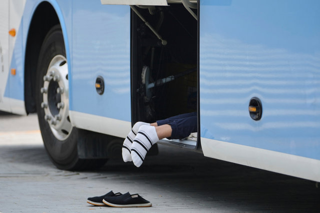 A bus driver takes a rest inside a luggage compartment, on a sweltering day, in Beijing, Tuesday July 22, 2025. (Photo by Andy Wong/AP Photo)