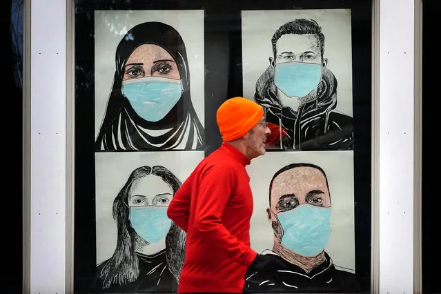 A runner passes by a window displaying portraits of people wearing face coverings to help prevent the spread of the coronavirus, Monday, November 16, 2020, in Lewiston, Maine. An executive order by Gov. Janet Mills' requires Maine citizens to wear face coverings in public settings, regardless of the ability to maintain physical distance. (Photo by Robert F. Bukaty/AP Photo)