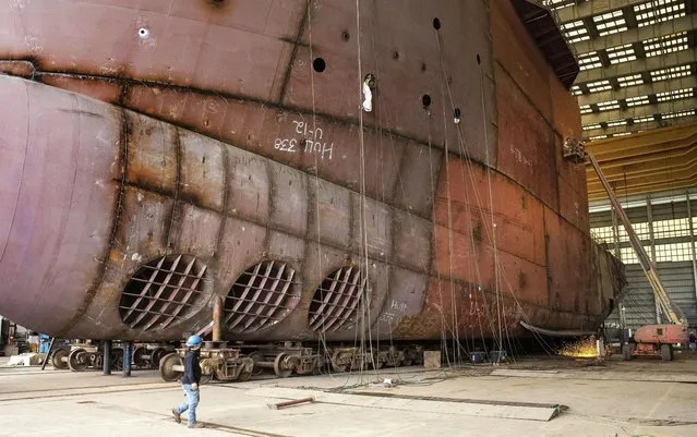A worker walks by an unfinished 260-foot-long Eco Edison ship in Terrebonne Parish, La., along the Houma Navigation Canal, Monday, April 3, 2023. The ship will serve as a floating housing for U.S. offshore wind technicians and a warehouse for their tools as they operate and maintain wind farms. (Photo by Ted Jackson/AP Photo)