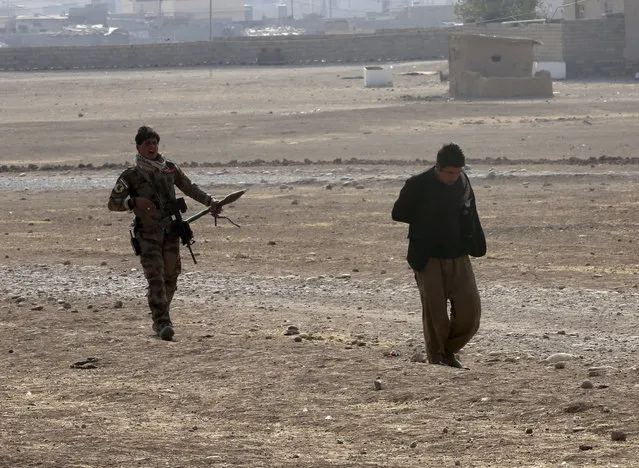 A member of Iraq's elite counterterrorism forces follows an arrested and handcuffed suspect of Islamic State in the village of Tob Zawa, about 9 kilometers (5½ miles) from Mosul, Iraq, Tuesday, October 25, 2016. Iraqi forces battled Islamic State fighters for a third day in a remote western town far from Mosul on Tuesday, but the U.S.-led coalition insisted the latest in a series of “spoiler attacks” had not forced it to divert resources from the fight to retake Iraq's second-largest city. (Photo by Khalid Mohammed/AP Photo)