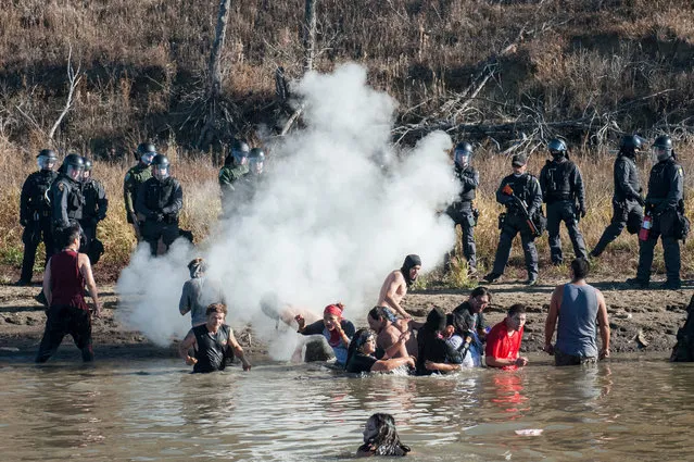 Police officers use tear gas against protesters standing in the water during a protest against the building of a pipeline near the Standing Rock Indian Reservation near Cannonball, North Dakota, U.S. November 2, 2016. (Photo by Stephanie Keith/Reuters)