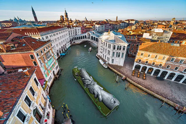 An aerial view shows an artwork by French-Swiss artist Saype called “Beyond Walls” on a floating barge, part of a series of interlocked hands as part of a project creating a spray-painted 'human chain' across the world to encourage humanity and equality, in Venice, Italy, April 15, 2022. (Photo by Valentin Flauraud for Saype/Handout via Reuters)