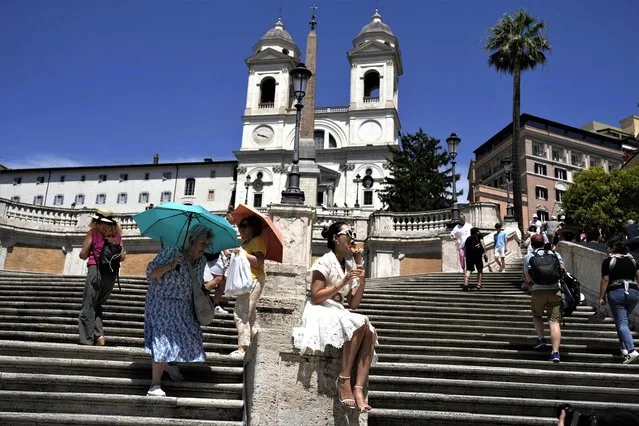 Tourists take shelter with umbrellas as another one enjoys an ice cream during a hot summer day at the Rome's Spanish Steps Thursday, July 6, 2023. (Photo by Alessandra Tarantino/AP Photo)