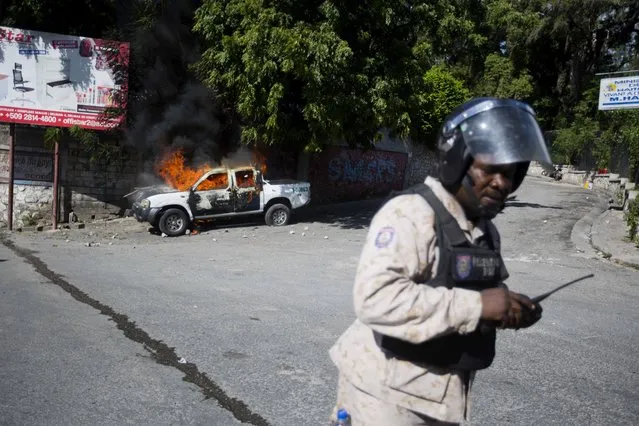 A national police officer stands near a police truck set on fire during an opposition protest demanding to know how Petro Caribe funds have been used by the current and past administrations, on the sidelines of events marking the 215th anniversary of independence Battle of Vertieres in Port-au-Prince, Haiti, Sunday, November 18, 2018. Much of the financial support to help Haiti rebuild after the 2010 earthquake comes from Venezuela's Petro Caribe fund, a 2005 pact that gives suppliers below-market financing for oil and is under the control of the central government. (Photo by Dieu Nalio Chery/AP Photo)