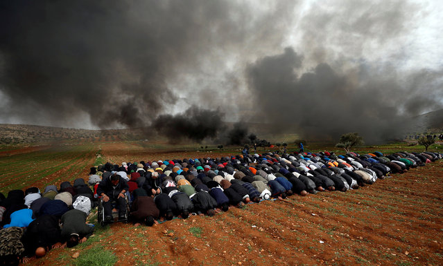 Palestinians perform Friday prayers as smoke rises from burning tires during a protest against Jewish settlements, in al-Mughayer village near Ramallah, in the Israeli-occupied West Bank, February 1, 2019. (Photo by Mohamad Torokman/Reuters)