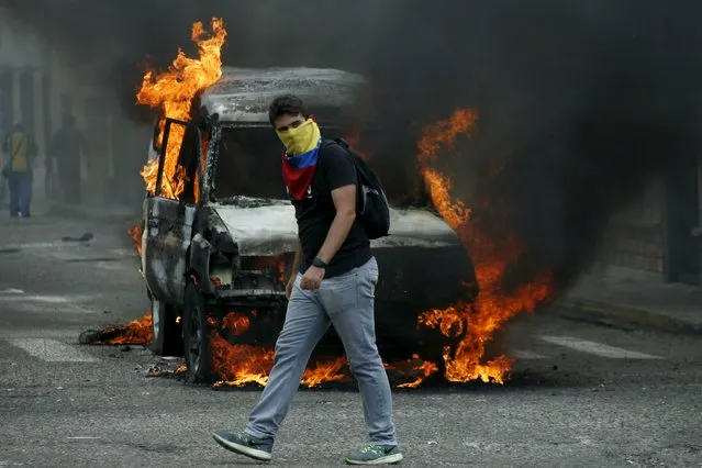 A demonstrator wearing a Venezuelan national flag to cover his face, walks in front of a burning van during a protest against President Nicolas Maduro's government in San Cristobal, Venezuela March 3, 2016. (Photo by Carlos Eduardo Ramirez/Reuters)