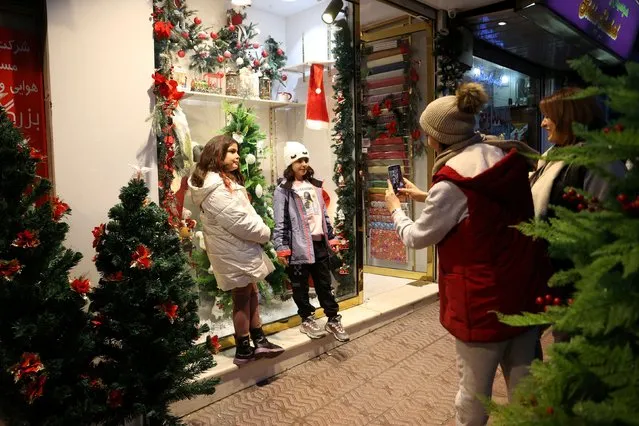 An Iranian woman takes a photo of her child in front of a Christmas shop in Tehran, Iran on December 25, 2023. (Photo by Majid Asgaripour/WANA (West Asia News Agency) via Reuters)