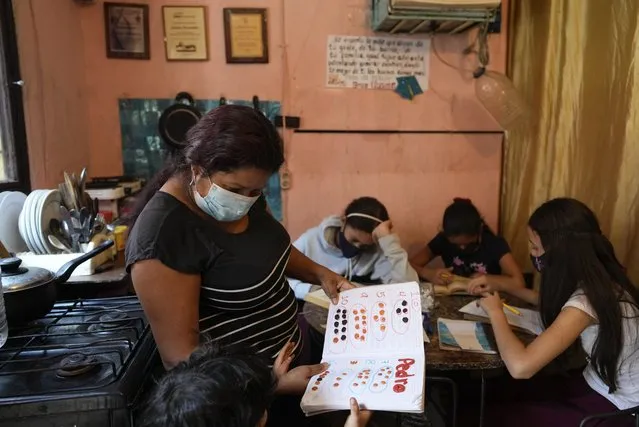 Teacher Johana Hernandez looks at a student's work in her one room home in Caracas, Venezuela, Wednesday, September 22, 2021. Hernandez, who lives with her husband and two children in a small home divided by curtains, opened her home to students while in-person school is on hold due to COVID-19 pandemic restrictions and to supplement her low teaching salary, which she says is not enough to live on. (Photo by Ariana Cubillos/AP Photo)