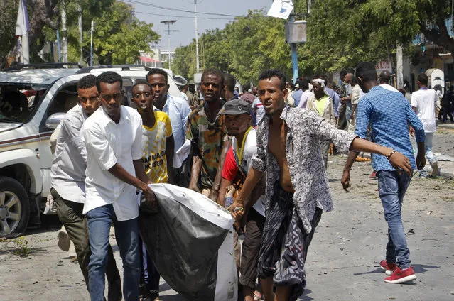 Somalis carry away a man who was wounded after blast outside a restaurant in Mogadishu, Somalia,  Thursday, March 28, 2019. A Somali police officer says an explosives-laden vehicle has detonated outside a restaurant in Somalia's capital, Mogadishu. (Photo by Farah Abdi Warsameh/AP Photo)