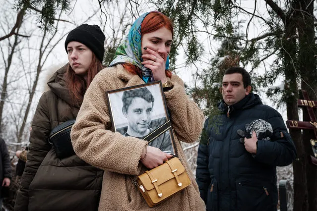 Kateryna Avdeyeva (C), mourns as she holds a portrait of her late friend, Ukrainian serviceman of the Azov battalion killed in action in Bakhmut, 28-year-old orphan Oleksandr Korovniy, as she attends his funeral ceremony at a cemetery in Sloviansk on January 30, 2023, amid the Russian invasion of Ukraine. (Photo by Yasuyoshi Chiba/AFP Photo)