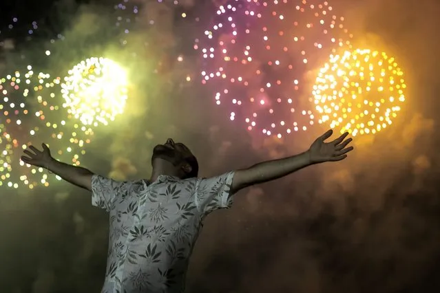 A man celebrates the start of the New Year, backdropped by fireworks exploding in the background over Copacabana Beach in Rio de Janeiro, Brazil, Saturday, January 1, 2022. (Photo by Bruna Prado/AP Photo)
